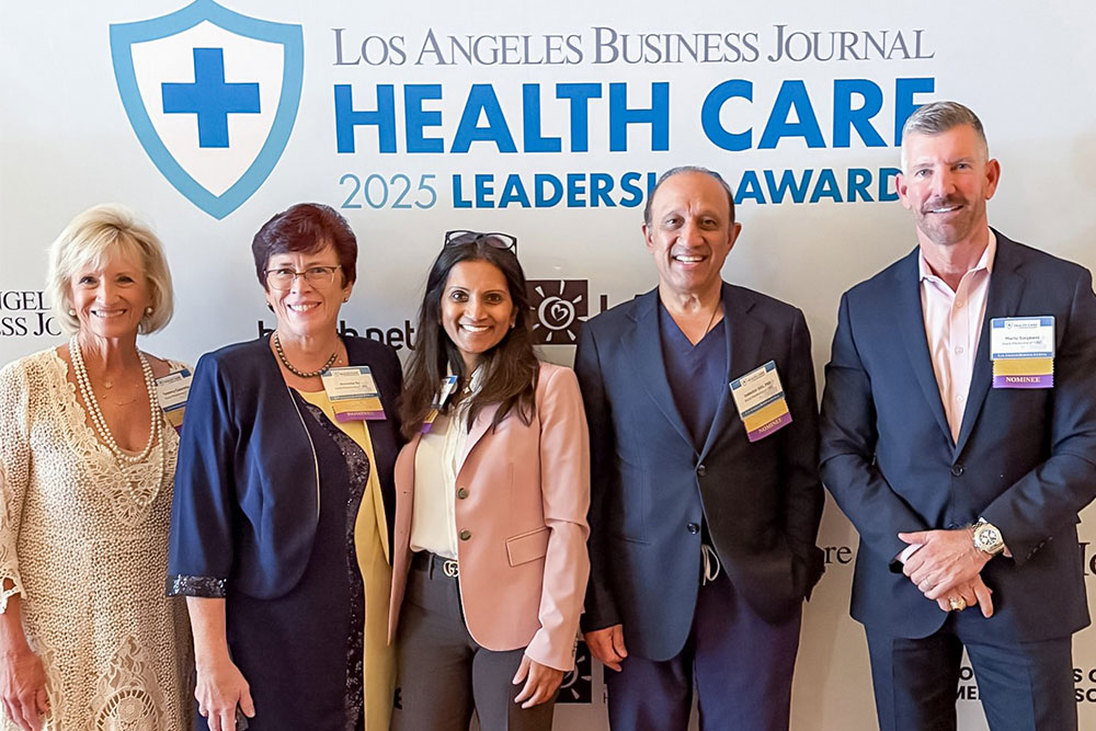 three women and two men stand in front of a step and repeat